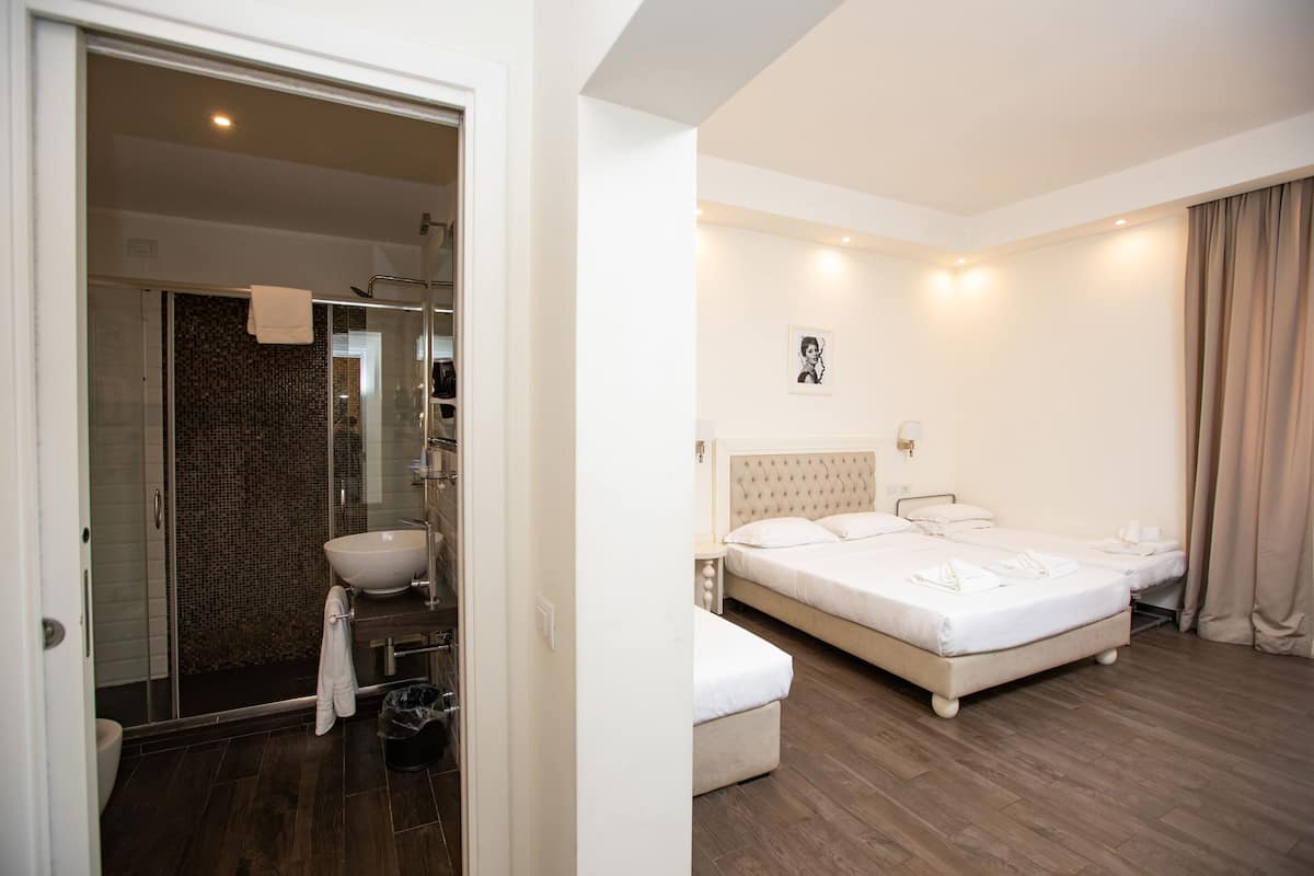 A hotel room with a large bed, a bathroom with a glass shower enclosure, and a white sink.