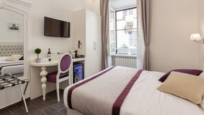 A hotel room with a bed, a desk, a chair, a television, and a window with curtains. - Relais Monti (Rome)