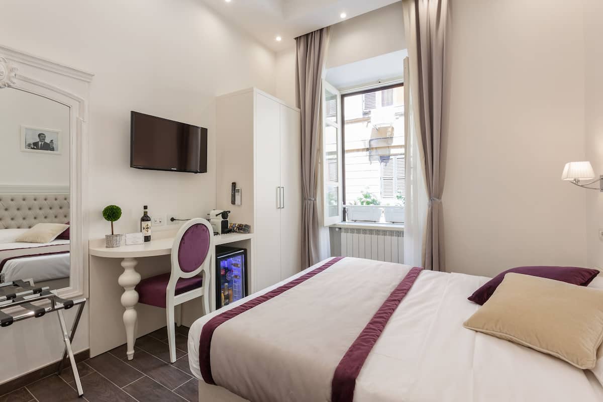 A hotel room with a bed, a desk, a chair, a television, and a window with curtains.