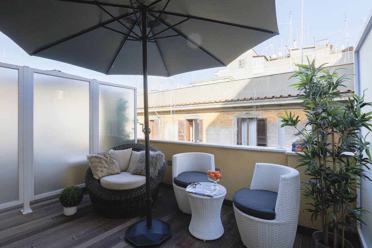 A balcony with wicker furniture, a potted plant, and a large umbrella.