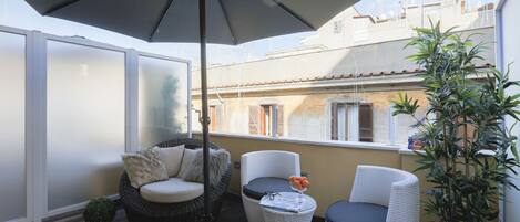 A balcony with wicker furniture, a potted plant, and a large umbrella.