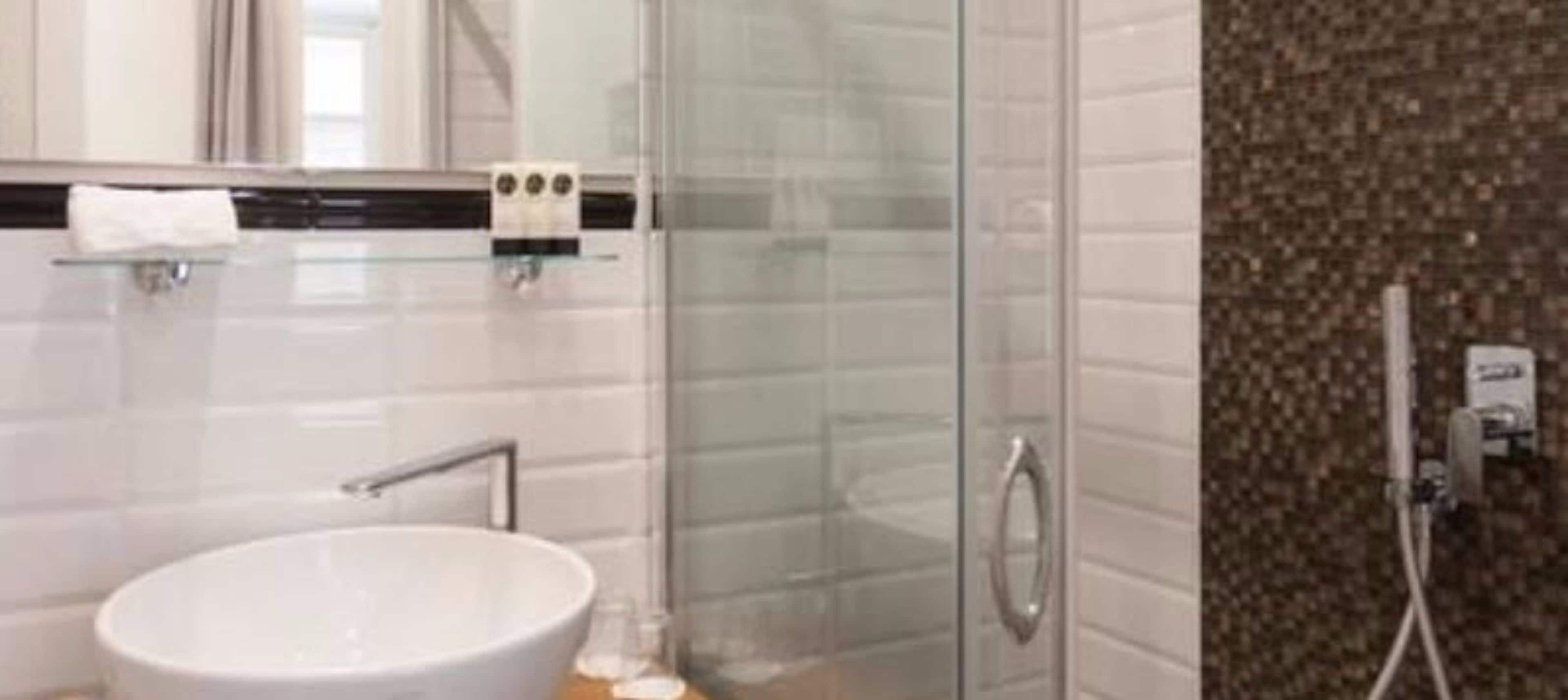 A modern bathroom with a glass shower enclosure, a white sink, and a towel rack.