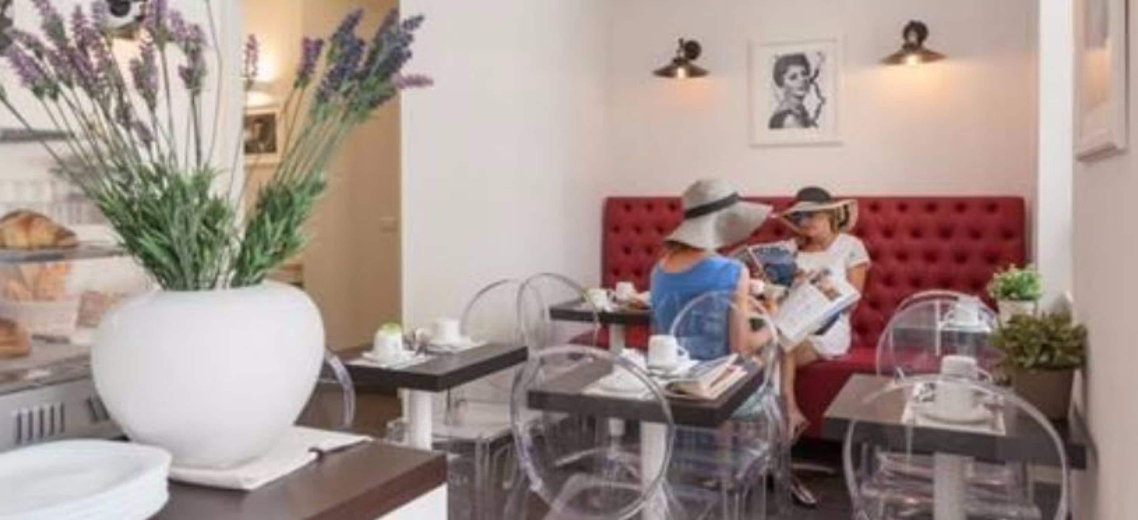 A restaurant with clear glass tables and chairs, a red upholstered booth, and a large white vase with lavender.