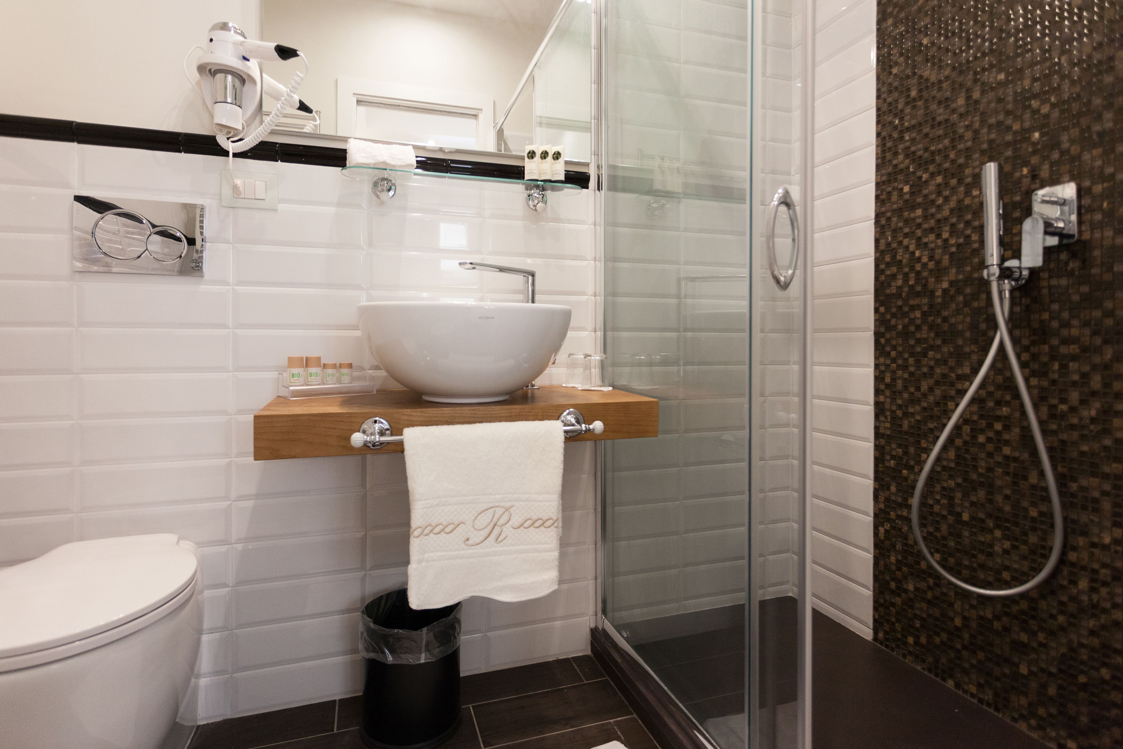 Un baño moderno con un lavamanos blanco, cabina de ducha de vidrio y un cubo de basura negro.