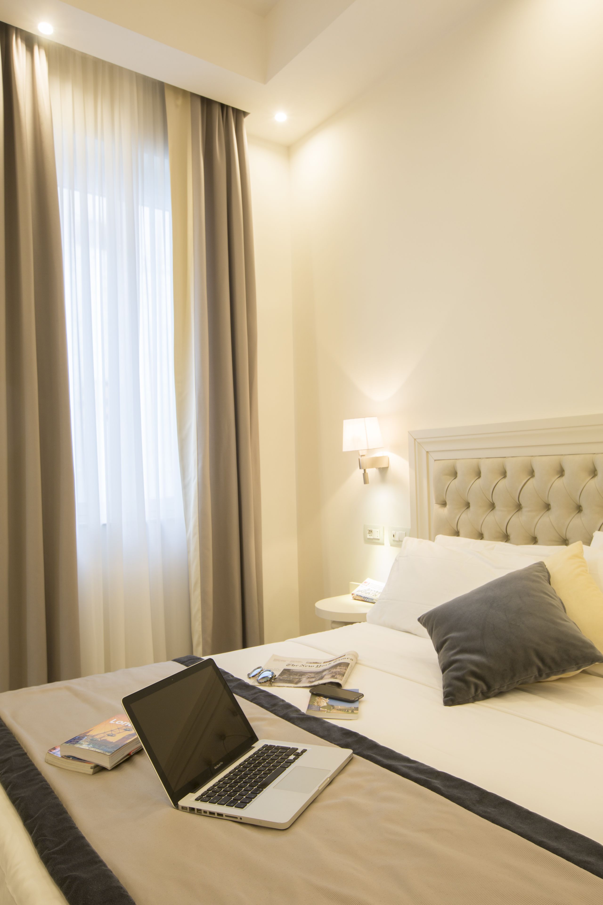 Et hotelværelse med seng, computer, lampe og et vindue med gardiner.
