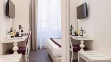A hotel room with a bed, two bedside tables, a TV, and a window with curtains.