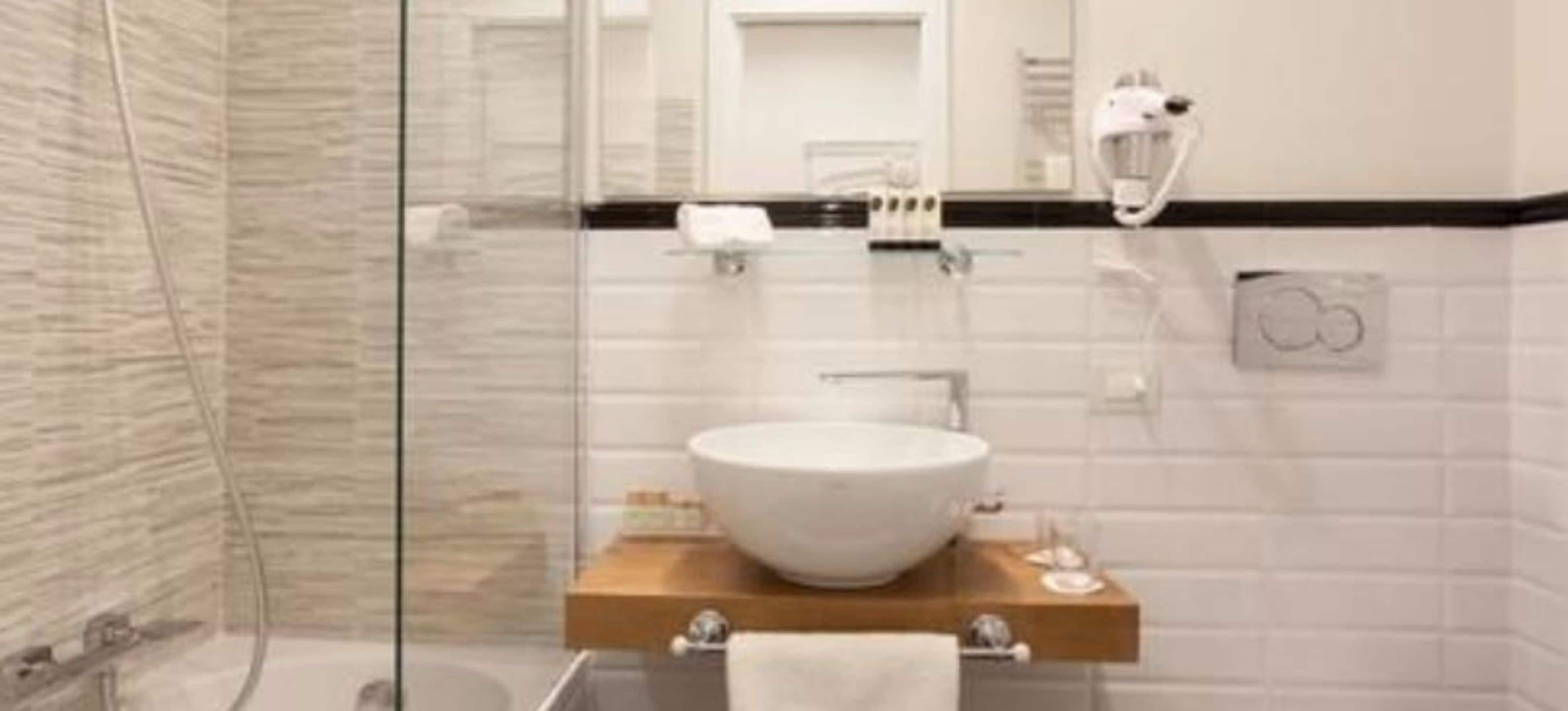 A modern bathroom with a glass shower enclosure, a large white sink, and a wooden vanity.