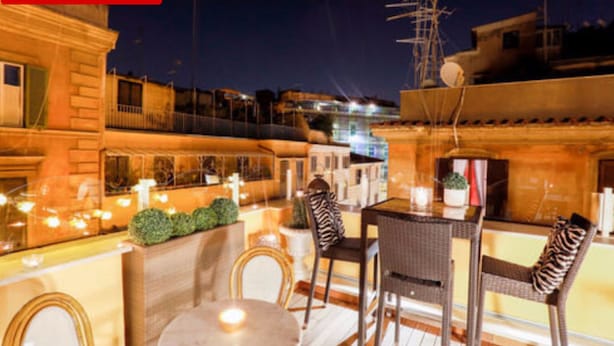 An outdoor seating area with wicker chairs and a table, surrounded by a low wall and potted plants. - Relais Monti (Rome)