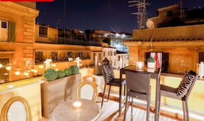 An outdoor seating area with wicker chairs and a table, surrounded by a low wall and potted plants. - Relais Monti (Rome)