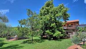 Un bâtiment en pierre avec un toit recouvert de tuiles rouges, entouré d’une pelouse bien entretenue et de grands arbres.