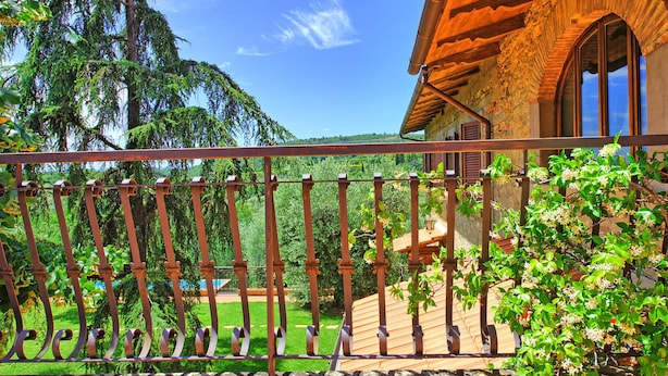 Une terrasse en bois avec une rambarde en métal, donnant sur un jardin luxuriant et un ciel d’un bleu éclatant.