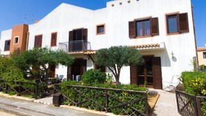 A white two-story house with brown shutters, a balcony, and a small garden. - Stagnone Holiday Apartment (Marsala)