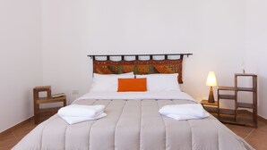 A neatly made bed with white and orange pillows, a wooden headboard, and a bedside lamp. - Stagnone Holiday Apartment (Marsala)