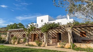 A traditional Mediterranean-style building with stone walls and wooden beams, featuring a central courtyard with a pergola and lush greenery. - Agroturismo Can Pujolet (Sant Antoni de Portmany)