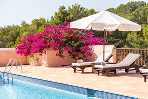 A poolside area with lounge chairs, a white umbrella, and vibrant pink bougainvillea flowers. - Agroturismo Can Pujolet (Sant Antoni de Portmany)