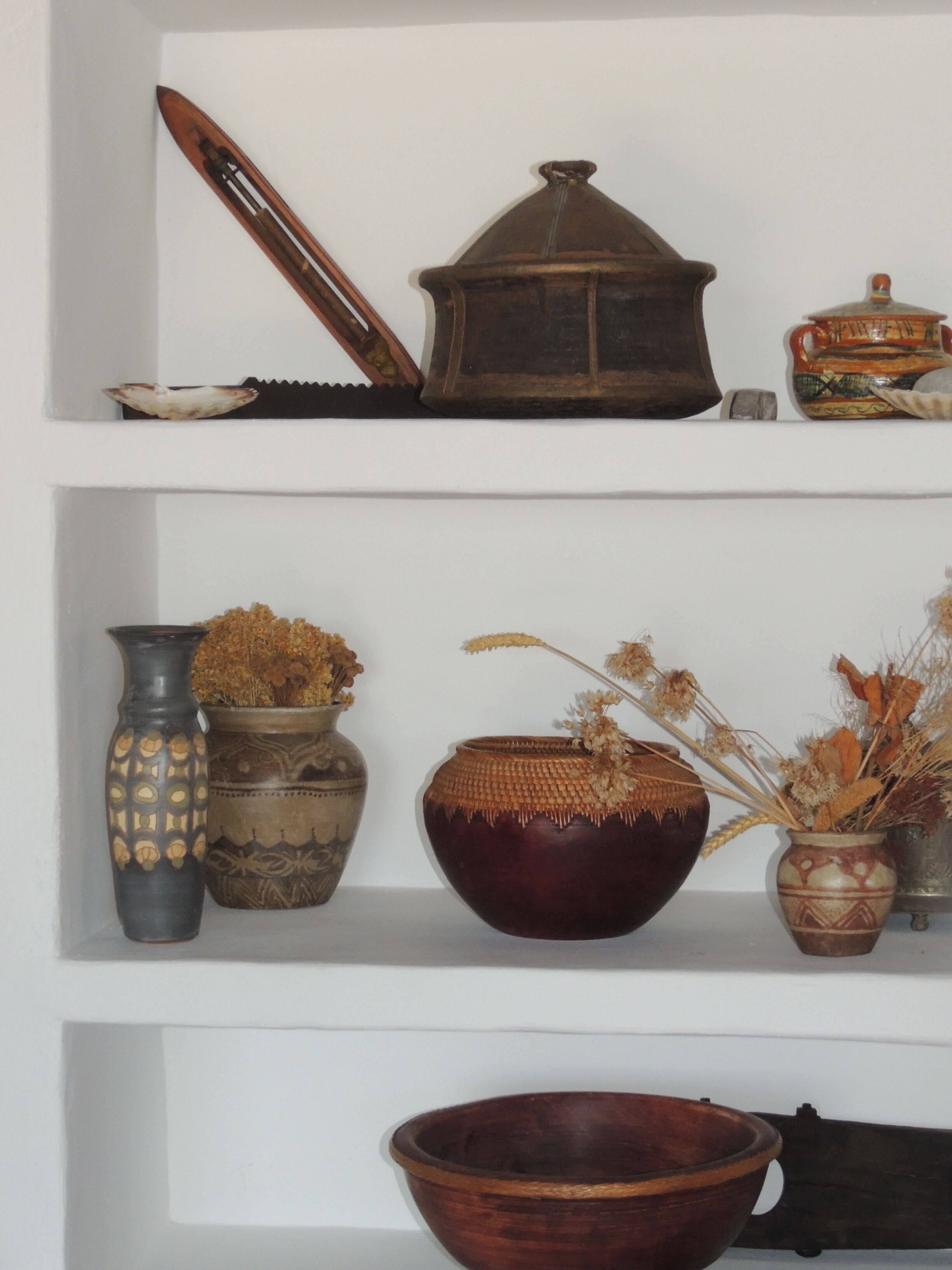 A shelf with various ceramic and wooden items, including a vase, a bowl, and a decorative piece.
