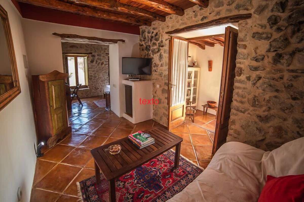 A cozy living room with a stone wall, a television on a stand, a wooden coffee table, and a red patterned rug.