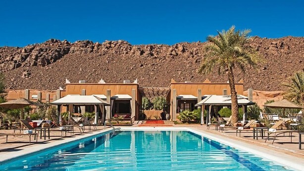 A swimming pool with lounge chairs and umbrellas, a building with a desert backdrop. - Hotel Bab Rimal (Foum Zguid)