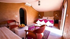 A room with a bed, two chairs, a small table with fruit, and a patterned rug. - Hotel Bab Rimal (Foum Zguid)