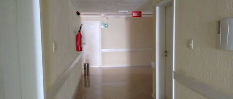 A hallway with a fire extinguisher mounted on the wall, a door at the end, and a light switch on the wall.