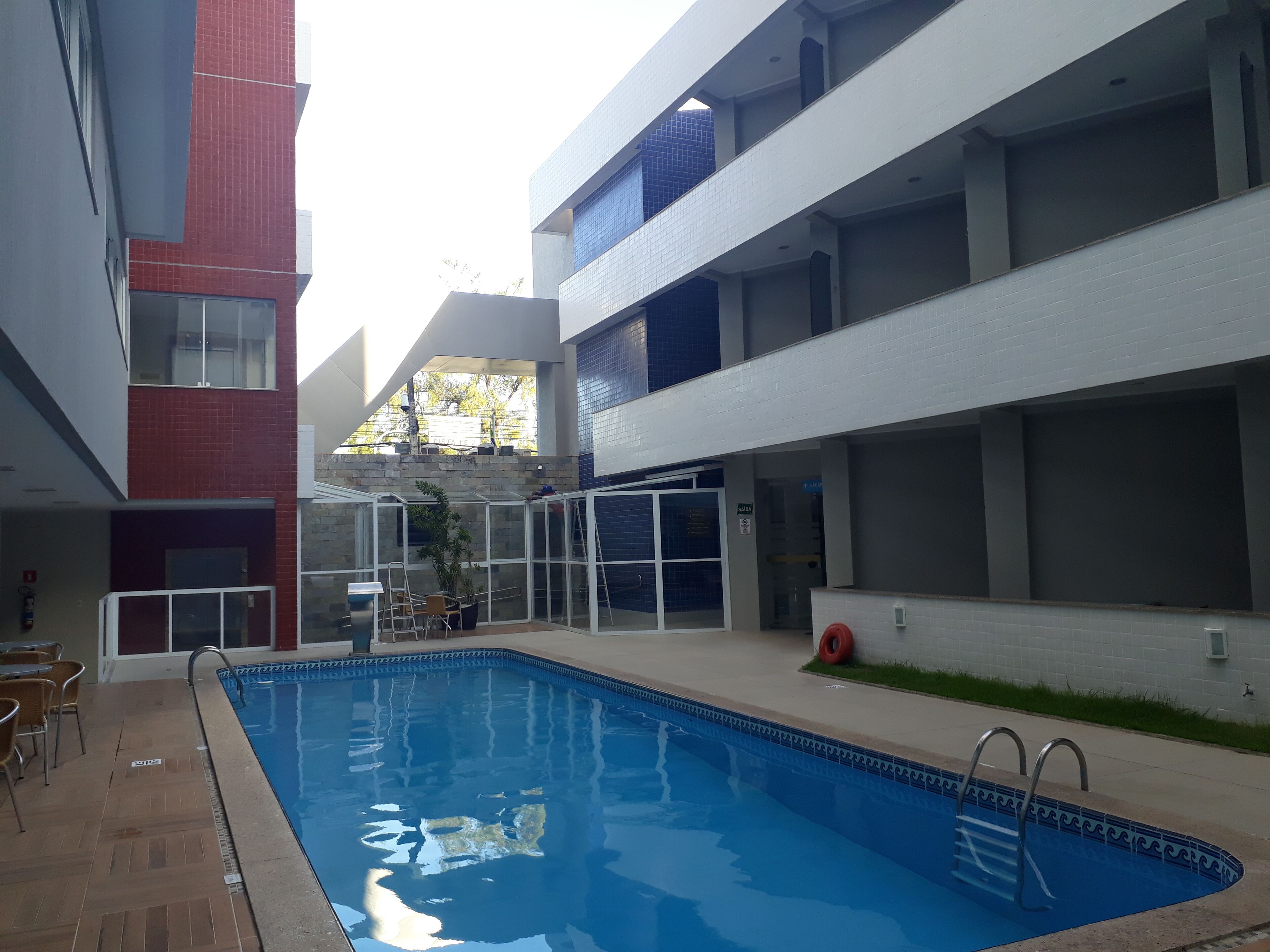 A swimming pool with a glass enclosure, surrounded by a building with multiple floors and a red brick facade.