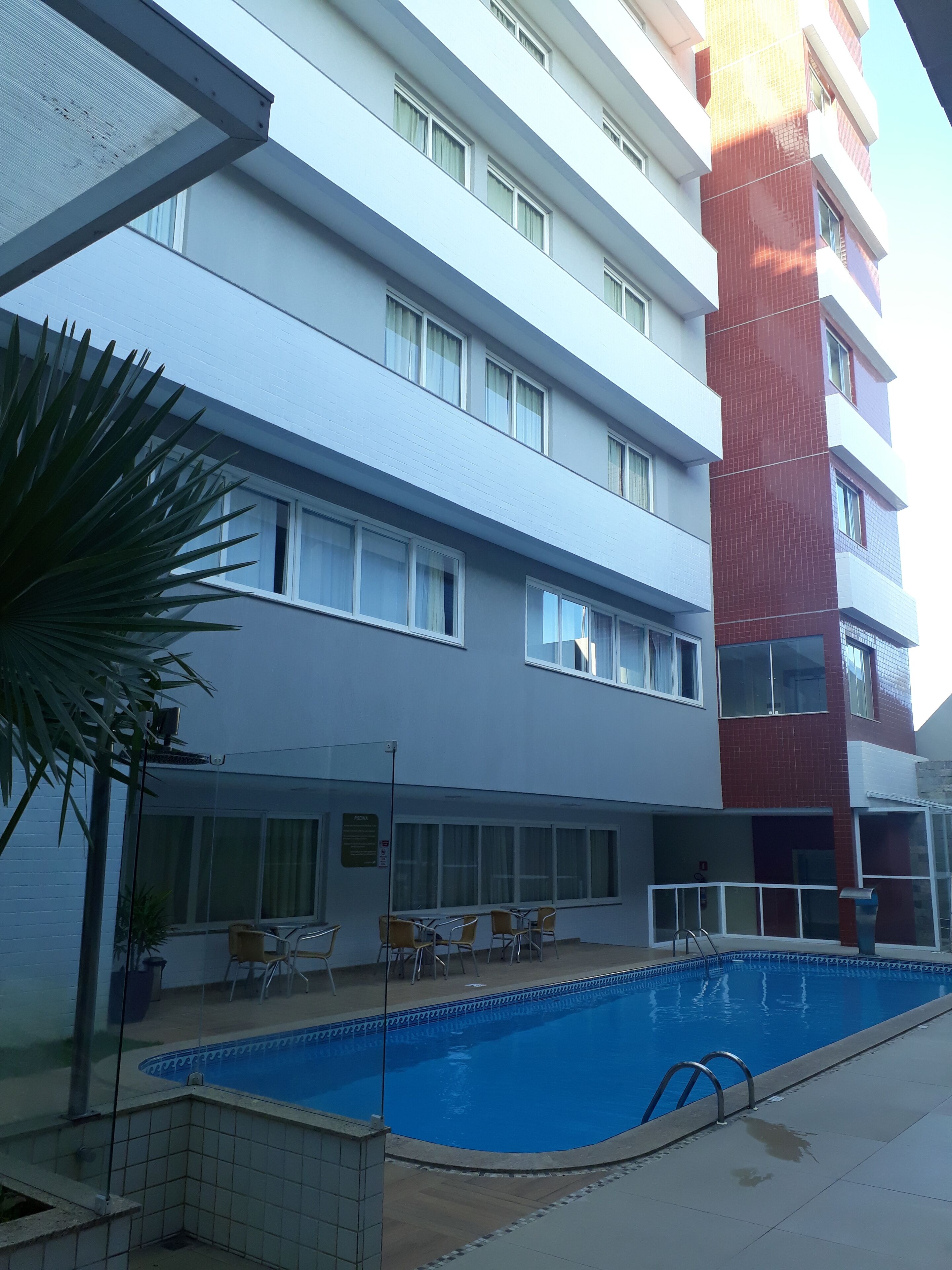 A hotel with a swimming pool, outdoor seating, and a red and white building facade.