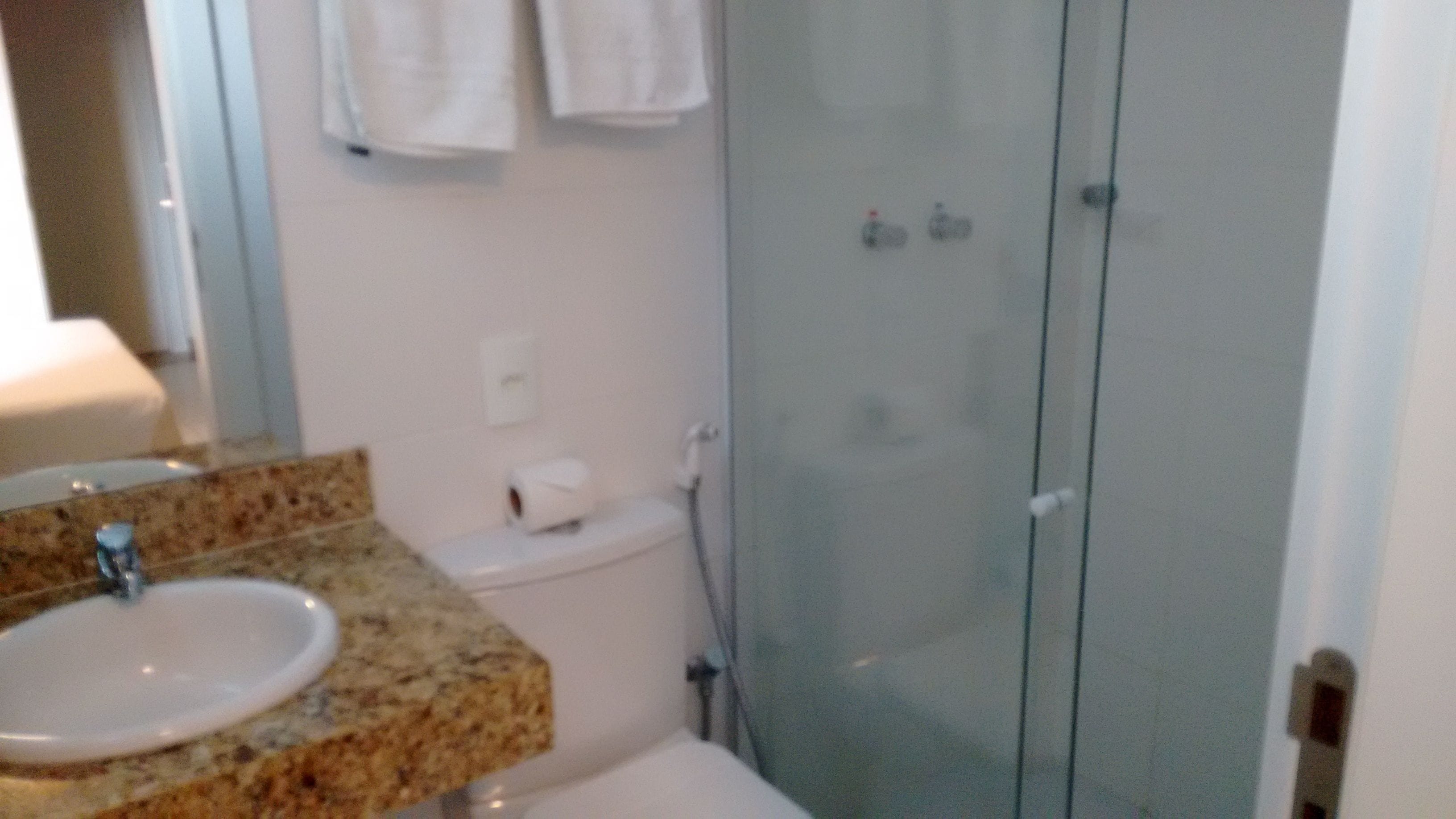 A bathroom with a granite countertop sink, a toilet, and a glass shower enclosure.