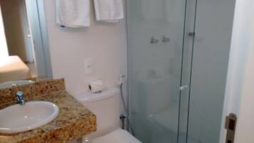 A bathroom with a granite countertop sink, a toilet, and a glass shower enclosure.