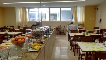 Un comedor de hotel con bufé, mesas, sillas y vistas al exterior a través de amplios ventanales.