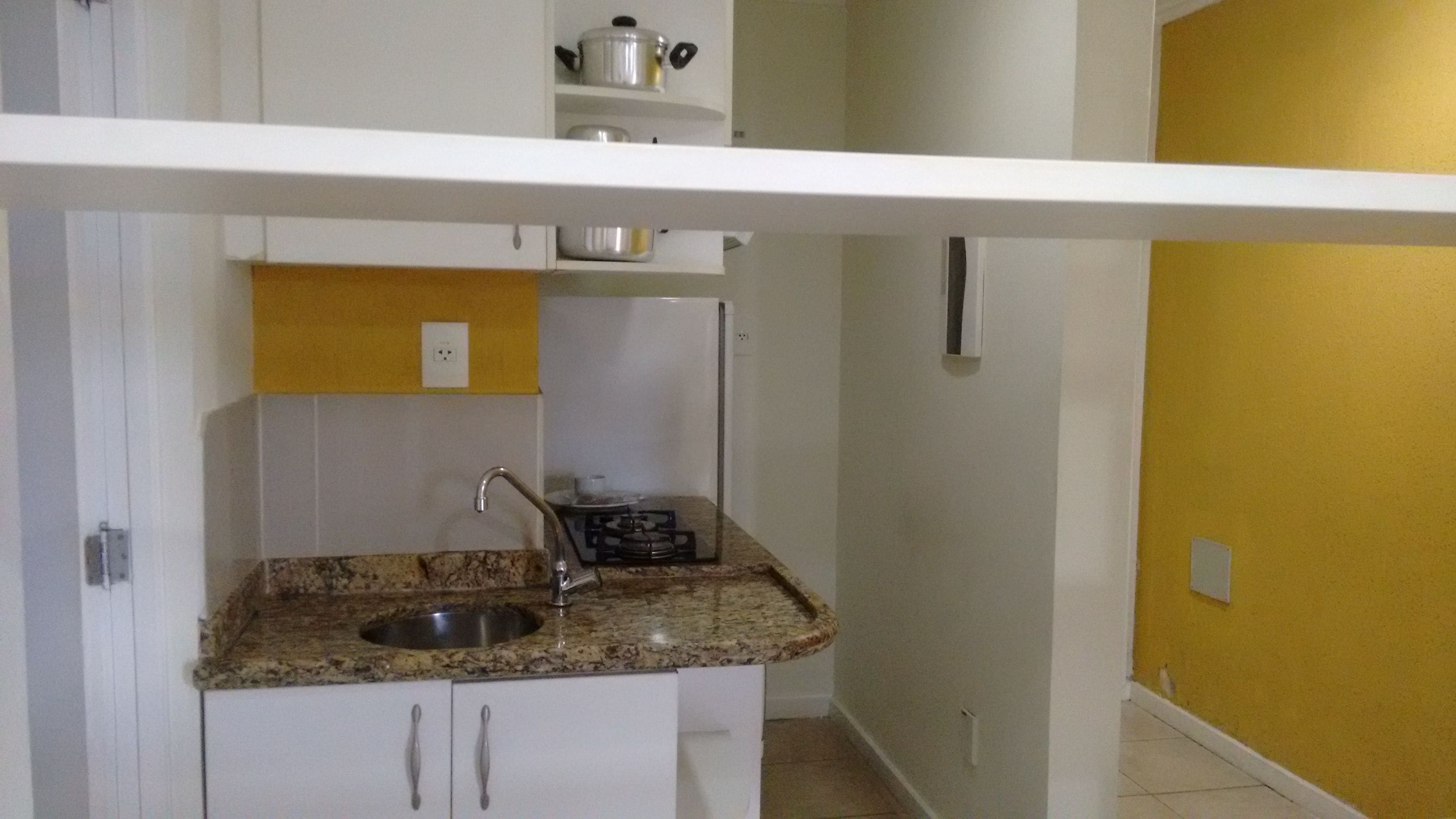Una cocina compacta con encimera de granito, pileta de acero inoxidable y armarios blancos.