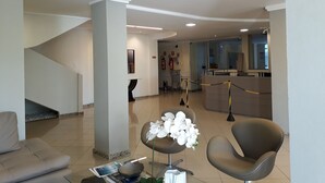 A lobby with a sofa, chairs, a reception desk, a staircase, and a flower arrangement. - Atalaia Apart Hotel (Aracaju)
