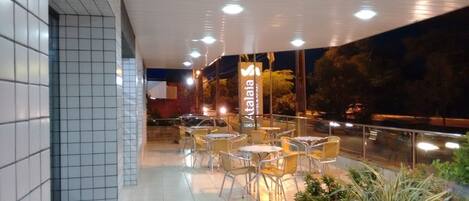An outdoor seating area with tables and chairs, a tiled wall, and a banner with the name "Atalaia".