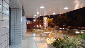 Un área de estar al aire libre con mesas y sillas, un muro de azulejos y un cartel con el nombre "Atalaia".