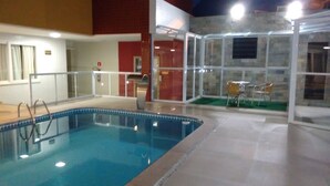 An indoor swimming pool with a clear glass enclosure, a tiled floor, and a seating area with chairs. - Atalaia Apart Hotel (Aracaju)