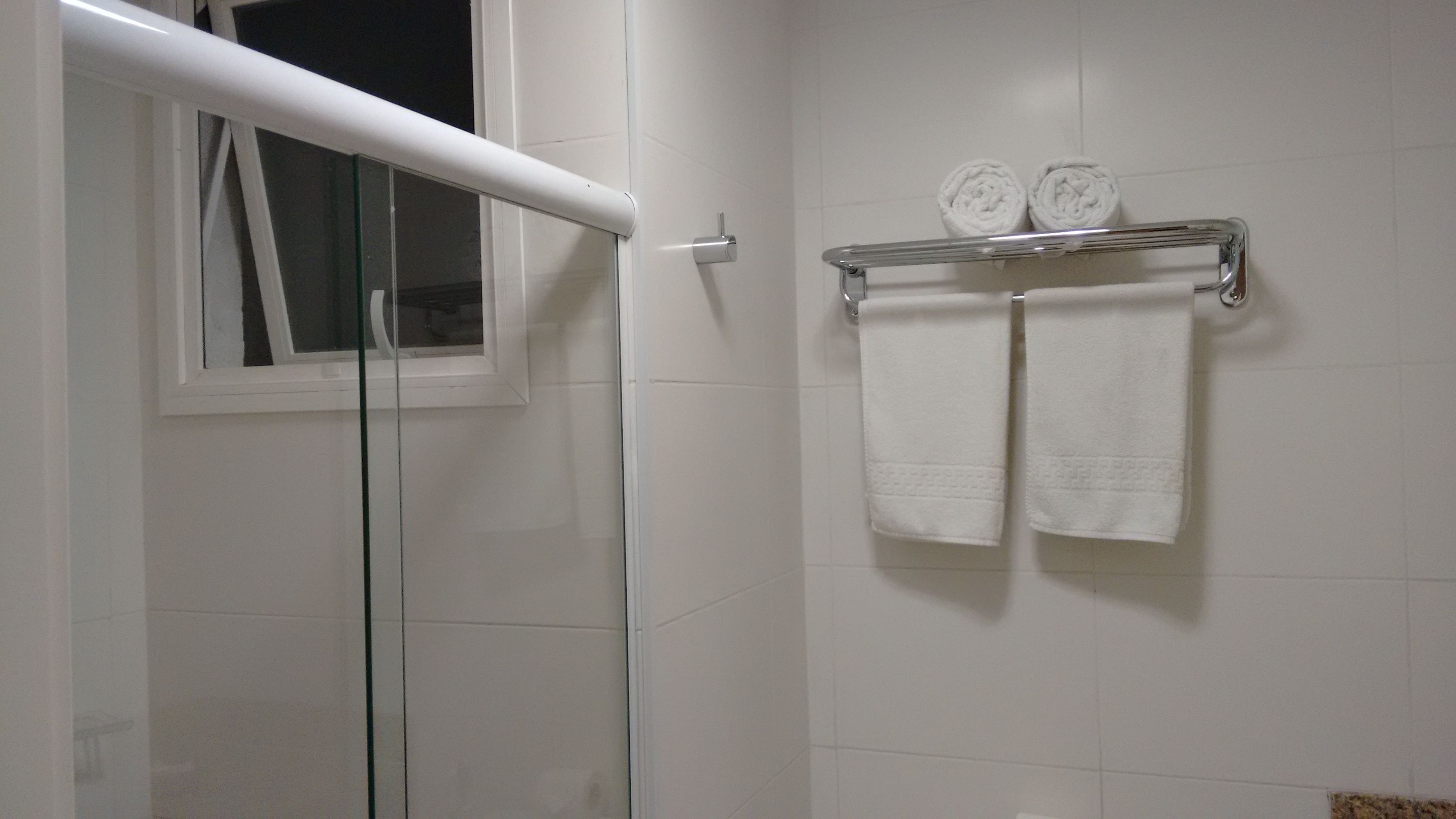A bathroom with white tiles, a glass shower enclosure, and a towel rack with two towels.