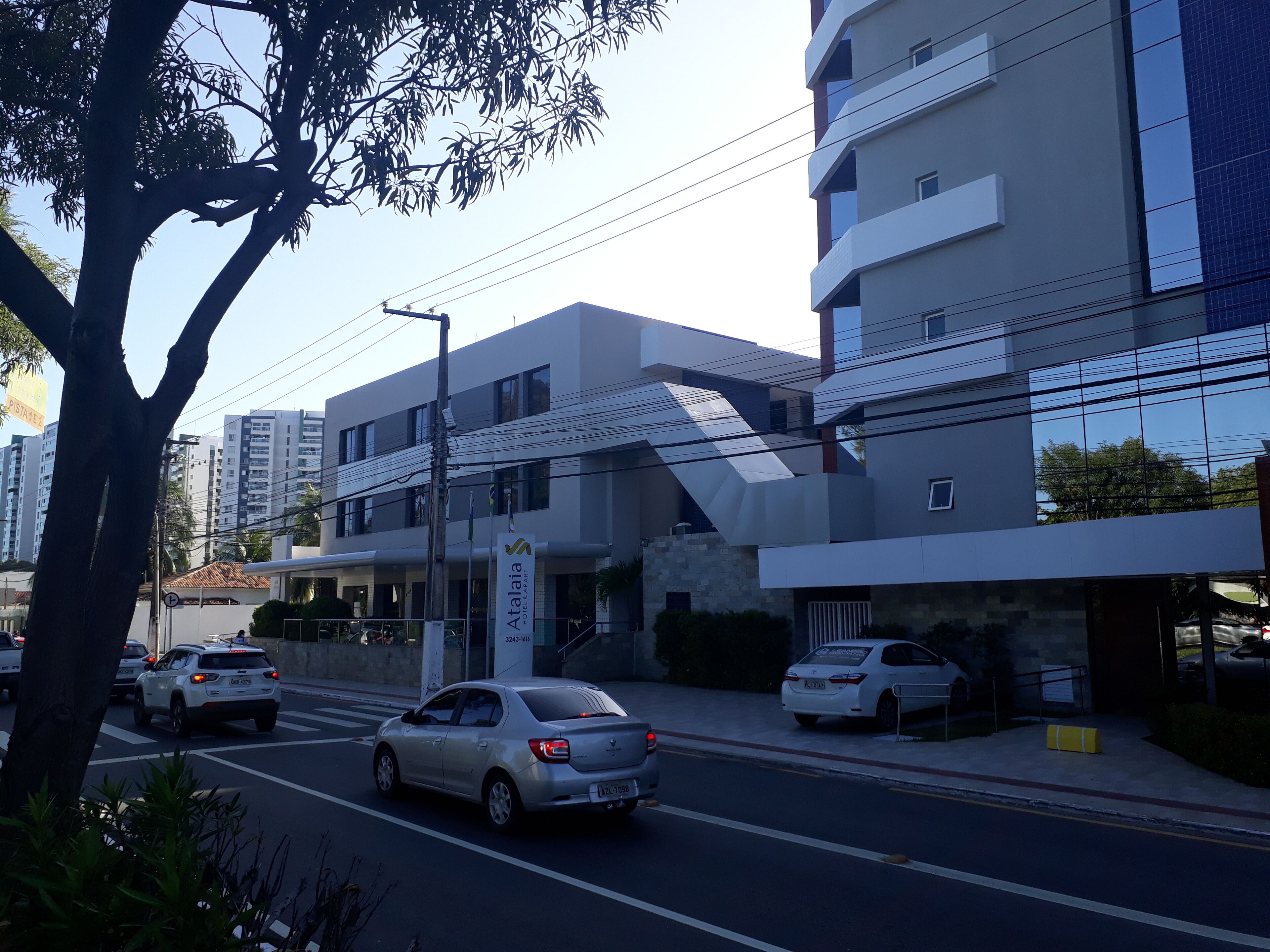 A modern building with a flat facade, a visible entrance, and a parking area with cars.