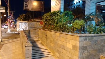 Vista nocturna de un edificio con muro de piedra y barandilla metálica. Se ven letreros de 'CANTON' y 'ATM'.