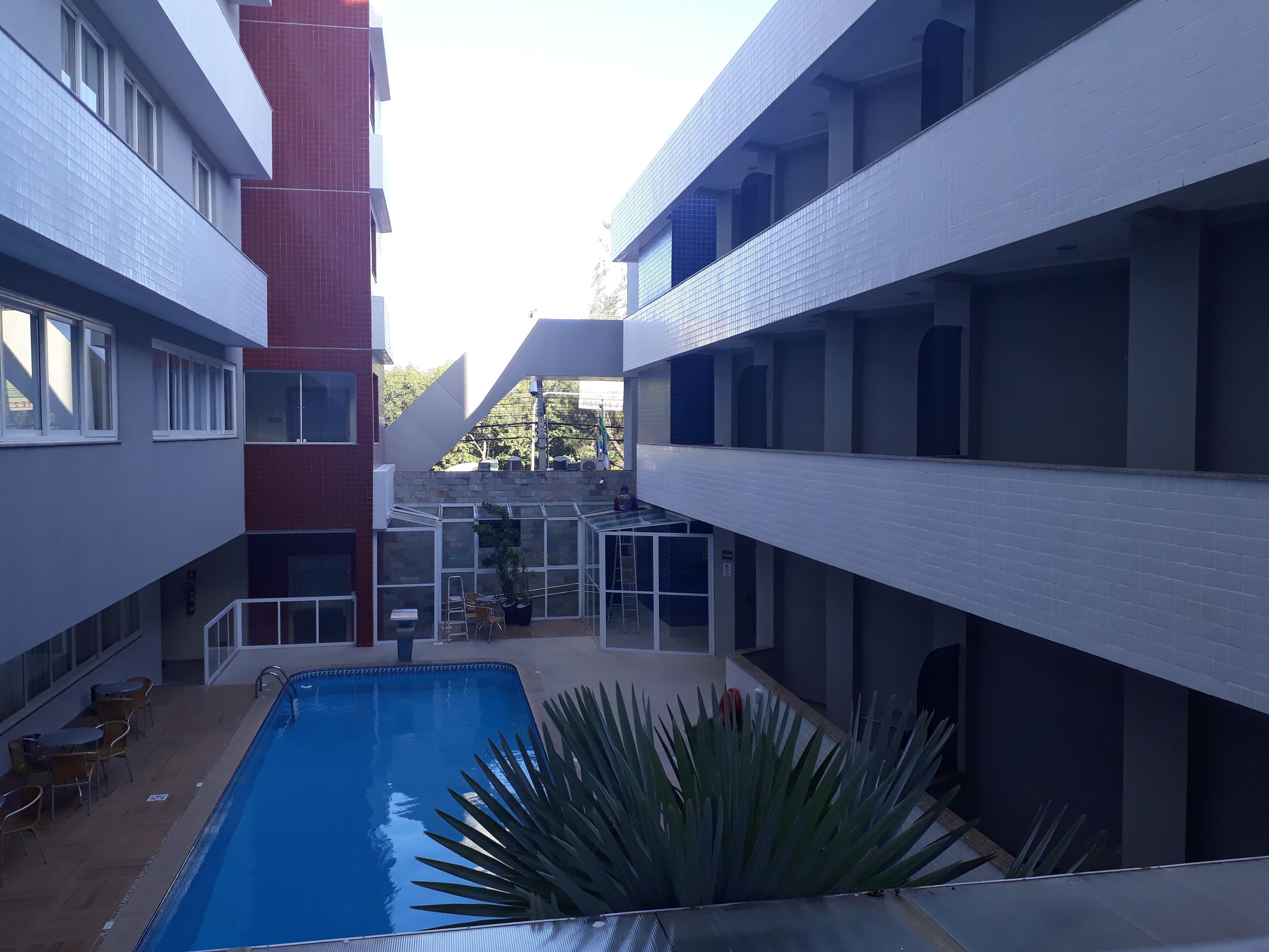 A modern building with a central courtyard featuring a swimming pool, surrounded by balconies and a red brick structure.