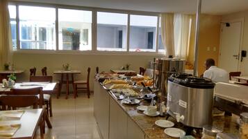 Un espace repas d’hôtel avec un buffet, comprenant une machine à café et un grand récipient en acier inoxydable portant l’inscription « LAIT FRAIS ».