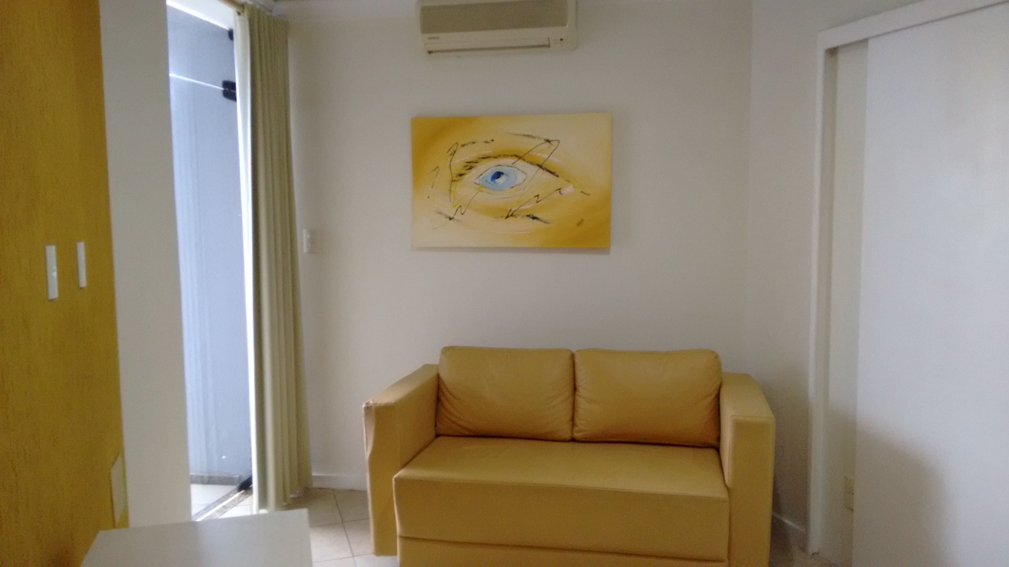 Una habitación con un sofá color crema, un cuadro de un ojo en la pared y una puerta con cortina.