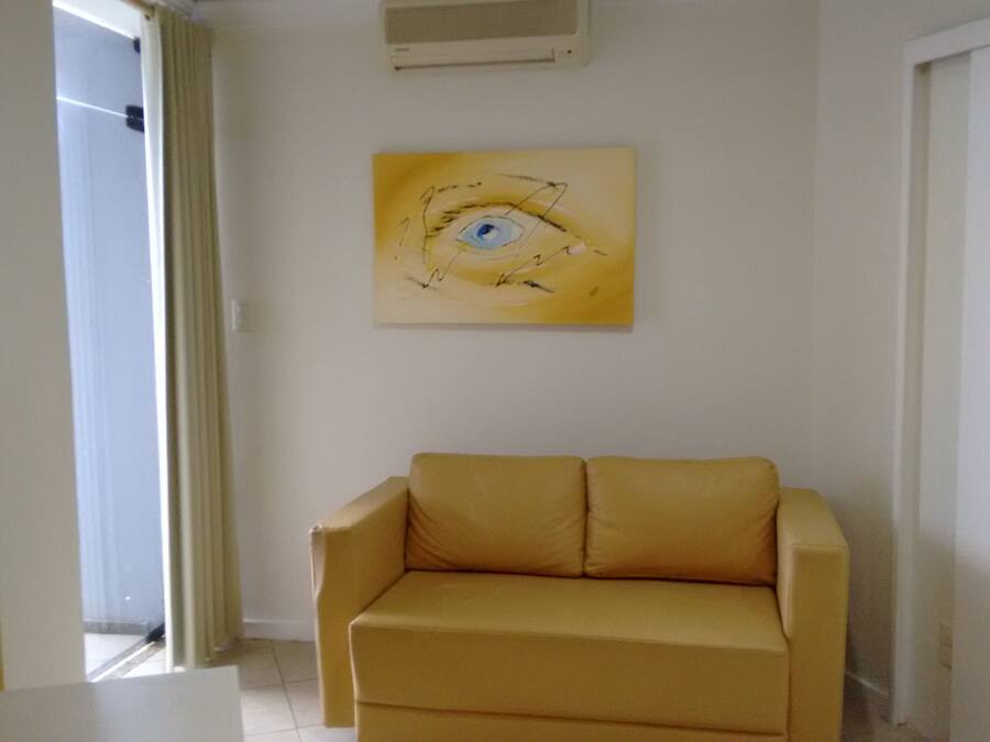 Una habitación con un sofá color crema, un cuadro de un ojo en la pared y una puerta con cortina.