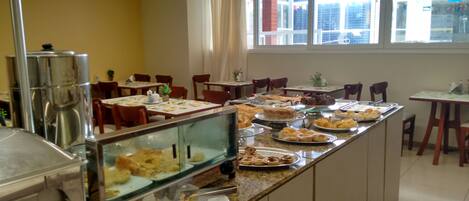 Zona de bufé con diferentes opciones de comida, una máquina de café y disposición de mesas.