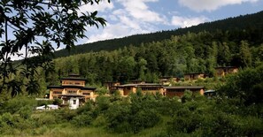 A cluster of traditional wooden buildings nestled in a forested hillside. - Naksel Boutique Hotel & Spa (Paro)