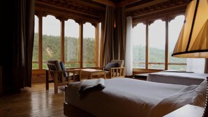 Une pièce de cabane en bois comprenant un lit, une chaise, une table et de grandes fenêtres donnant sur un paysage boisé.