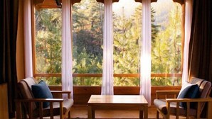 Une pièce chaleureuse avec une grande fenêtre, deux chaises en bois, une petite table et un tapis à motifs.