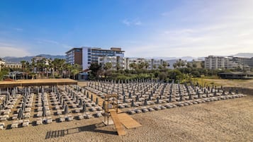 A beach with rows of sun loungers and umbrellas, a wooden deck, and buildings in the background.
