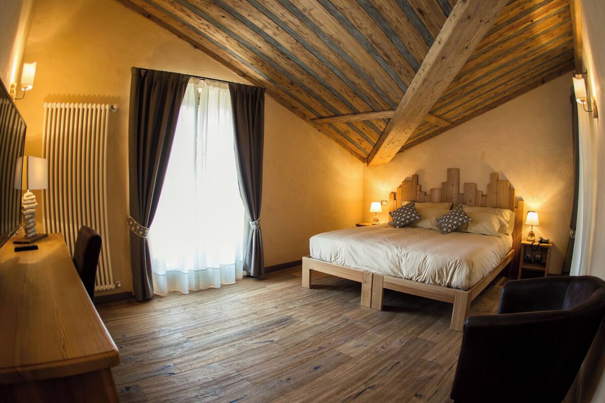 Una camera da letto con soffitto in legno, un letto con cuscini, una sedia, una scrivania e una lampada.