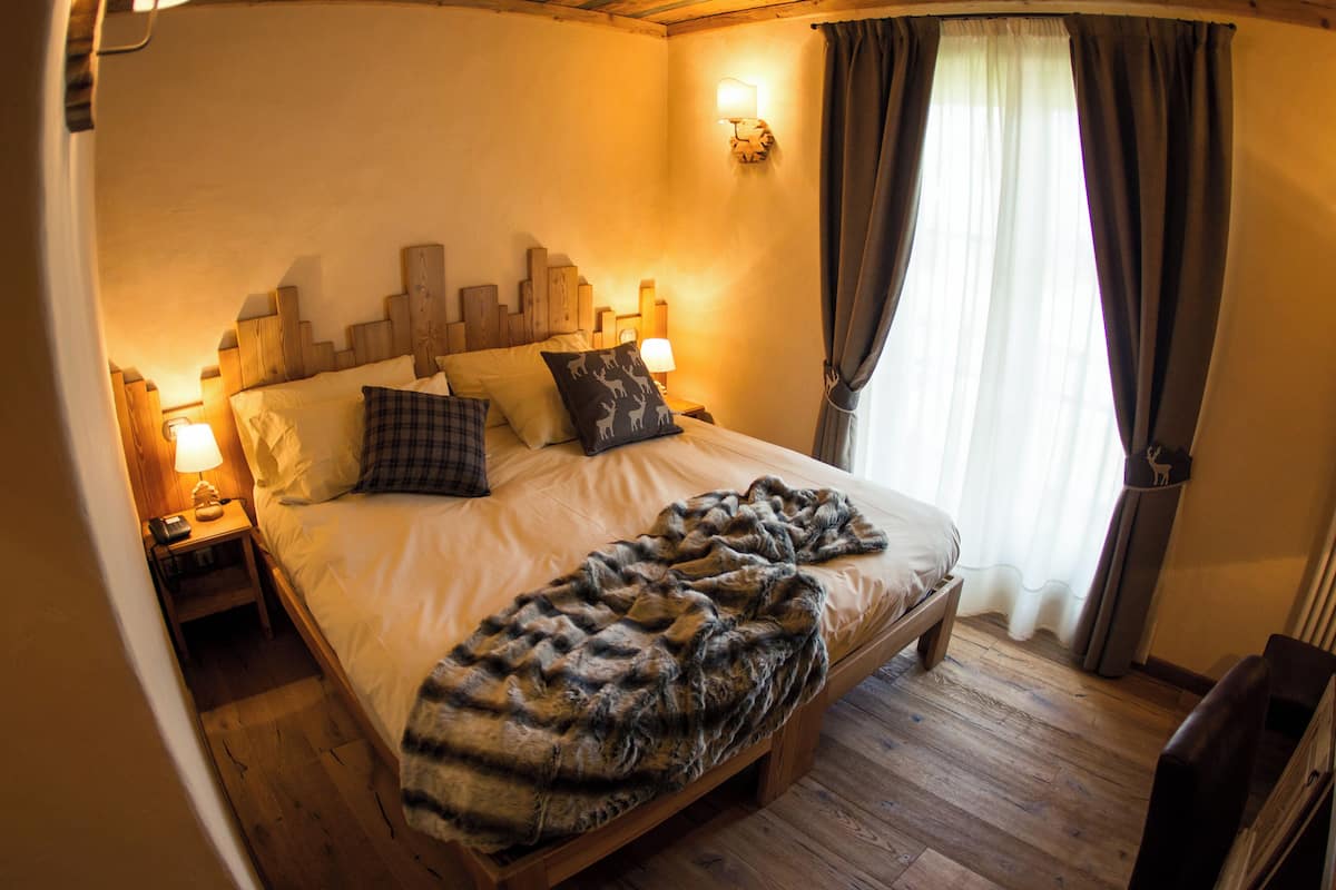 Una camera accogliente con una testiera di legno, un letto grande con una coperta in pelliccia sintetica, due lampade ai comodini e una finestra con tende.