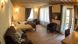 Una habitació amb un llit, un sofà, una cadira, una taula de fusta i una televisió penjada a la paret.