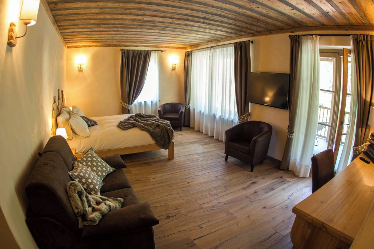 Una stanza con un letto, un divano, una sedia, un tavolo in legno e una TV montata a parete.